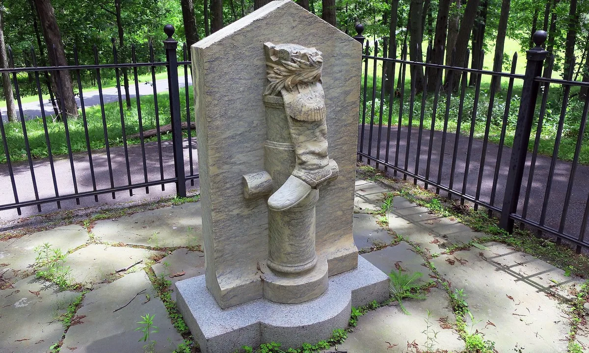 Small stone monument carved with a cannon barrel, an officer's boot and an eagle, standing in a grassy field.