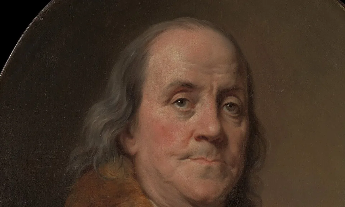 Oval portrait of an elderly man with long grey hair in a plain brown coat and white shirt against a dark background.
