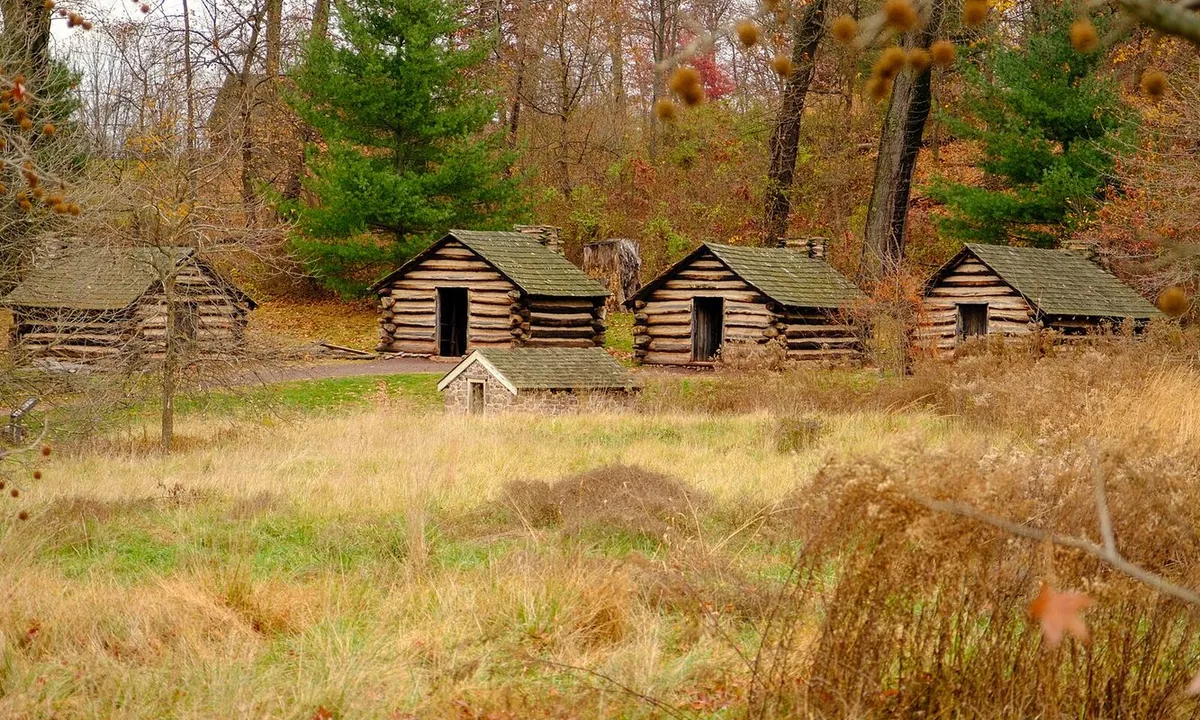 Row of small log cabins with clay-chinked walls and stone chimneys on a grassy slope.