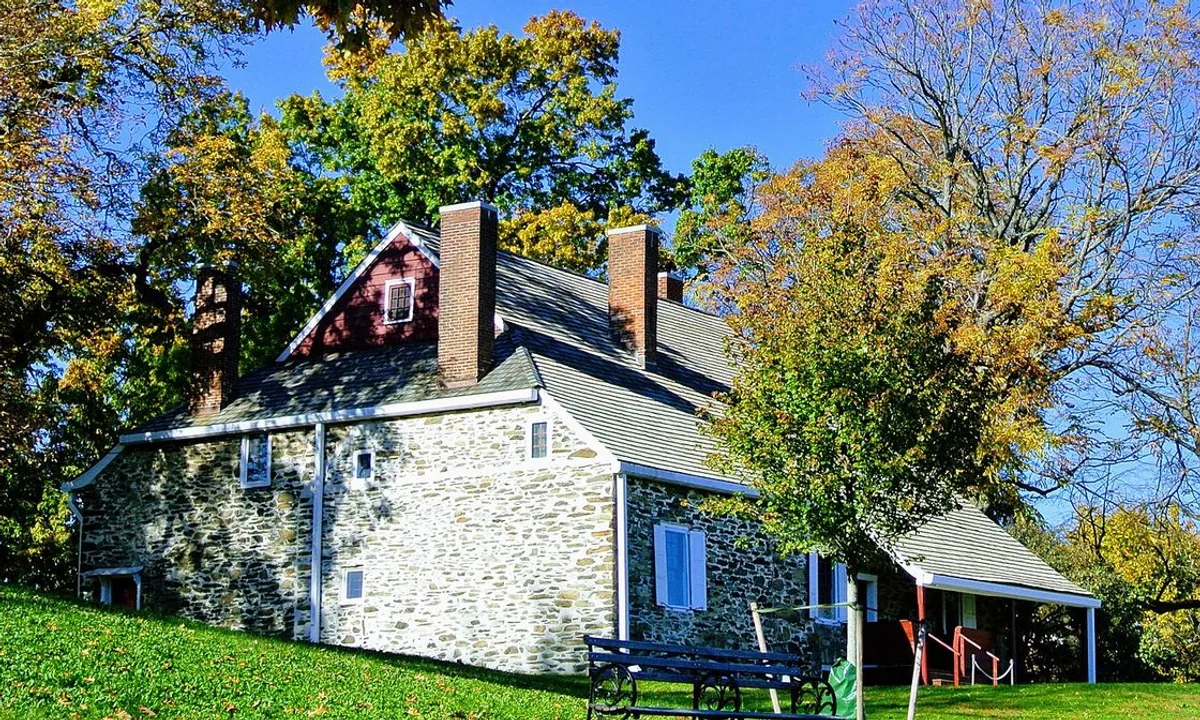 Low fieldstone farmhouse with a steep shingled roof on a lawn above a river valley.