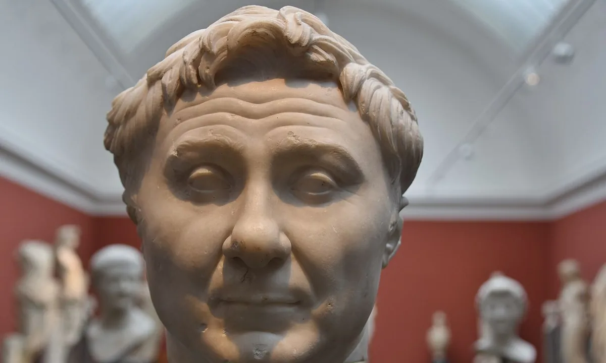 Marble head of a heavy-featured middle-aged man with a tuft of hair raised above his forehead.