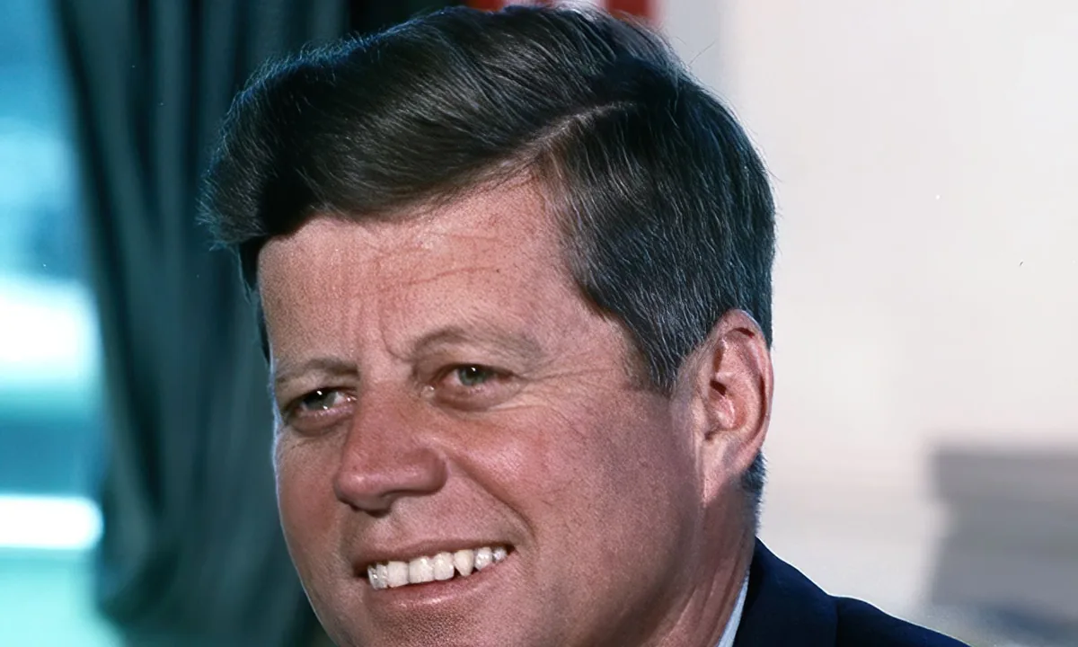 Colour portrait of Kennedy, smiling, in a dark suit and tie.