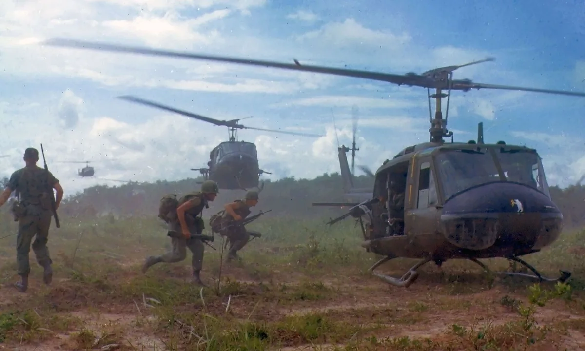 Colour photo of soldiers running from a landing helicopter as more helicopters come in over a field.