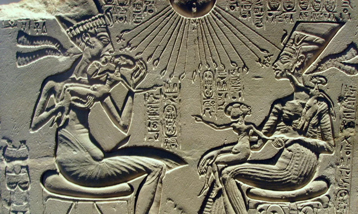 Limestone relief of a king and queen seated facing each other, playing with small children, under a sun disk with long rays ending in hands.