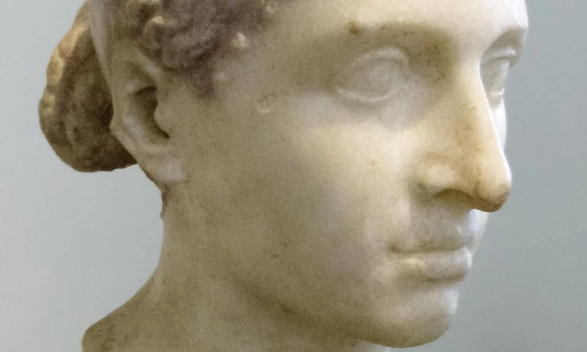 Marble head of a woman with her hair drawn back in ridged sections into a bun, and a flat band around her head.
