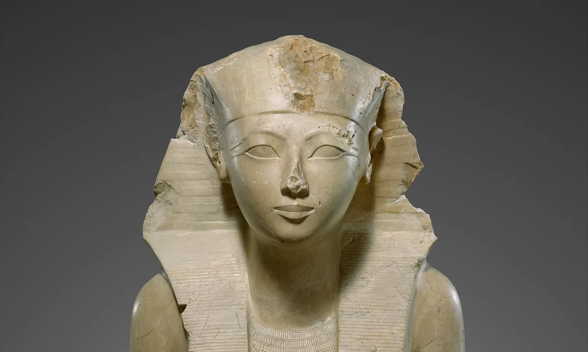 White limestone statue of a seated figure wearing a striped royal headcloth, with a slim body and hands resting on the knees.