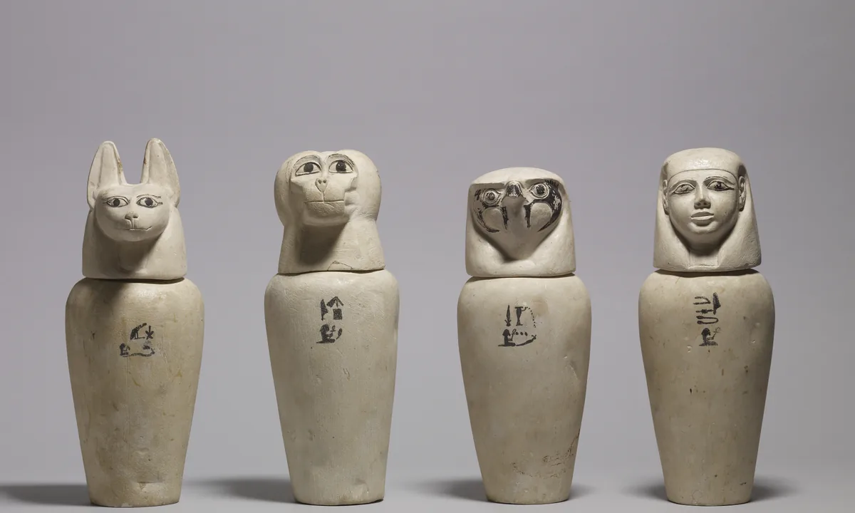 Four stone jars in a row with lids carved as a human head, a baboon head, a jackal head and a falcon head.