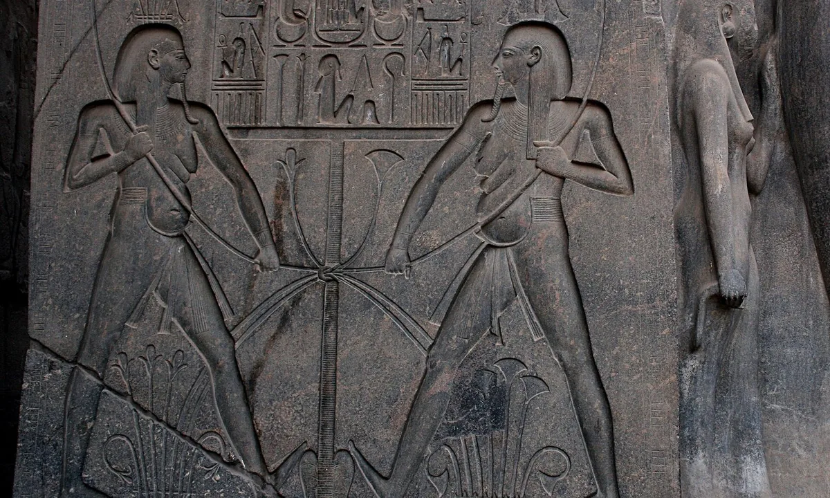 Carved stone showing a procession of small figures with standards, rows of headless bodies, and below them two long animal necks curling around a circular hollow.