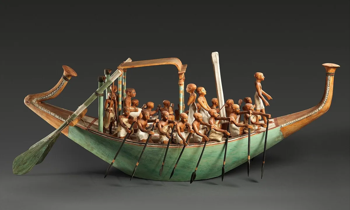Wooden model of a long boat with small painted figures of rowers and a canopy at the centre.