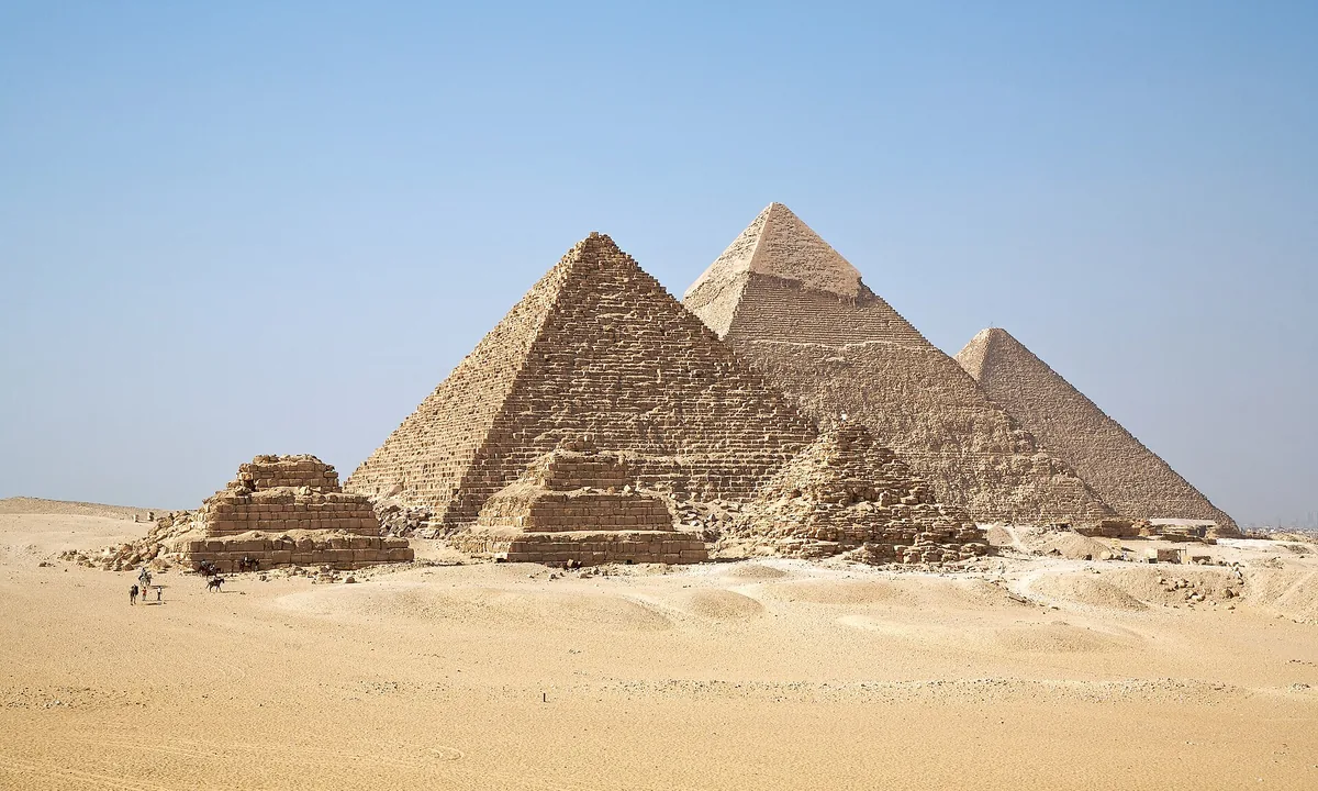 Three large pyramids and three small ones rising from the desert under a clear sky.
