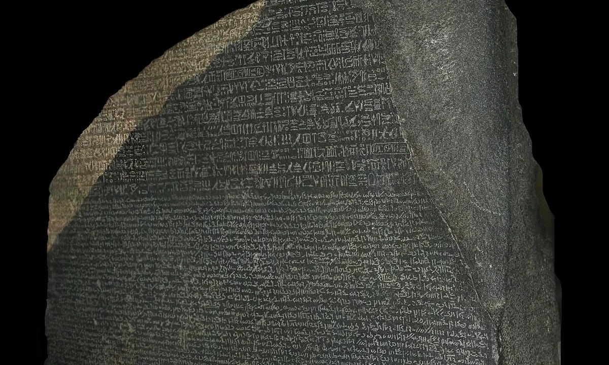 A dark grey stone slab with a broken top, covered in three bands of finely carved writing.