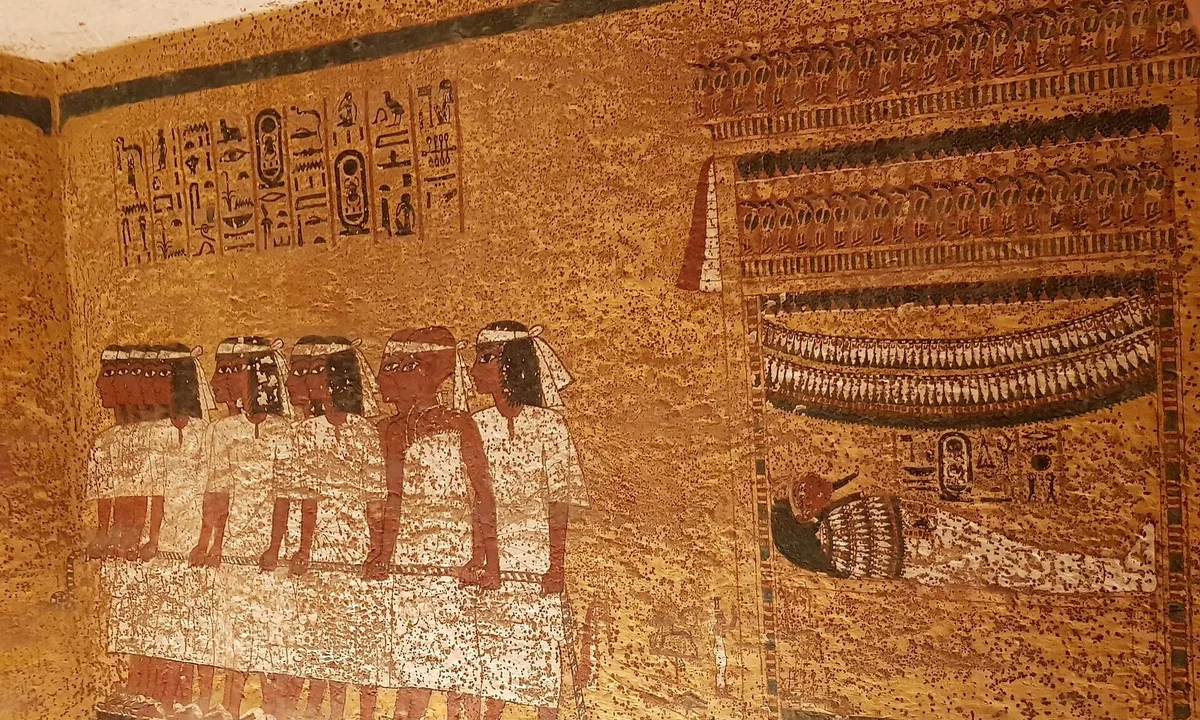Tomb painting on a yellow wall: a row of men in white kilts and headbands hauling, with hieroglyphs above.