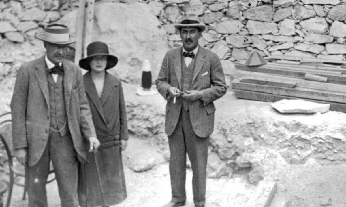 Black-and-white photograph of two men and a young woman in 1920s clothes standing beside a stone-lined pit in the desert.