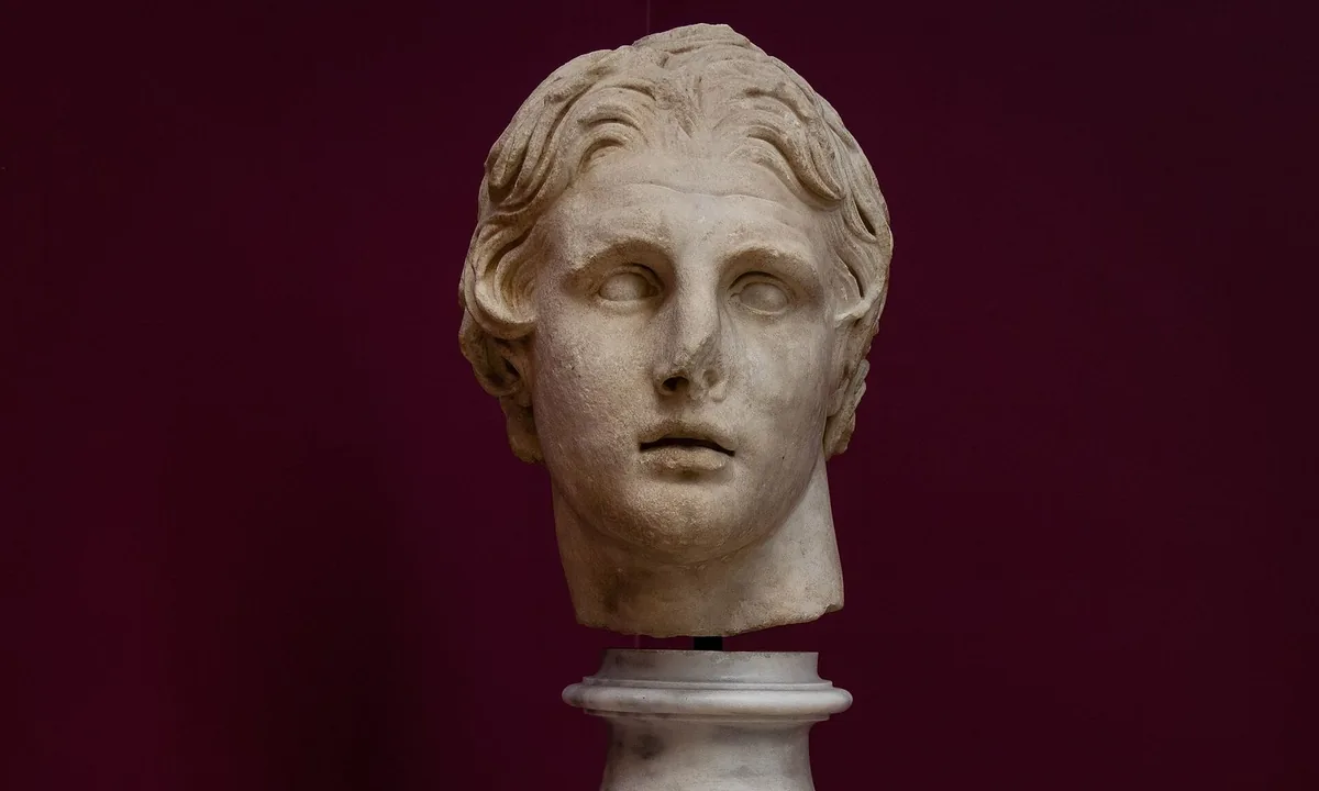 Marble head of a young man with thick, swept-back wavy hair, slightly parted lips and eyes turned upward, against a dark red wall.