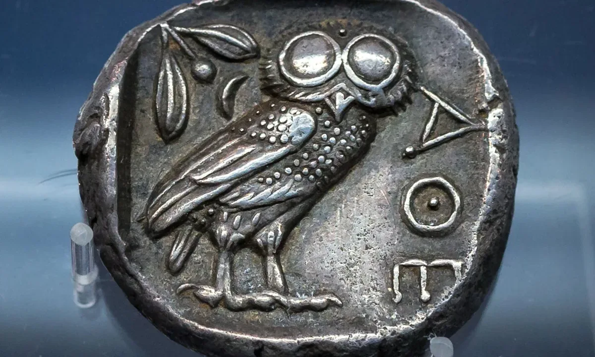 Silver coin showing an owl with large round eyes, an olive sprig and the Greek letters ΑΘΕ.