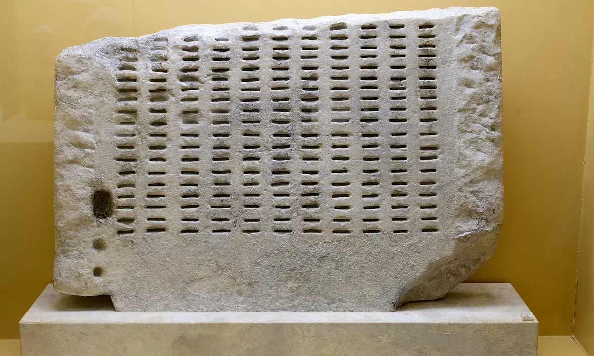 A marble slab covered in rows of narrow horizontal slots, displayed in a museum case.