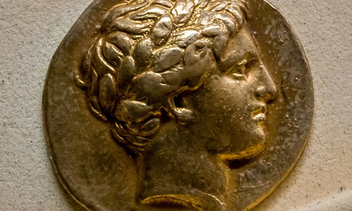 A gold coin showing the profile of a young man with short curly hair and a laurel wreath.
