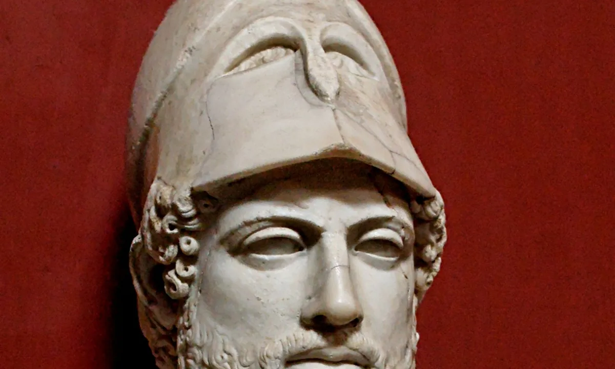 Marble herm bust of a bearded man wearing a Corinthian helmet pushed back on his head.