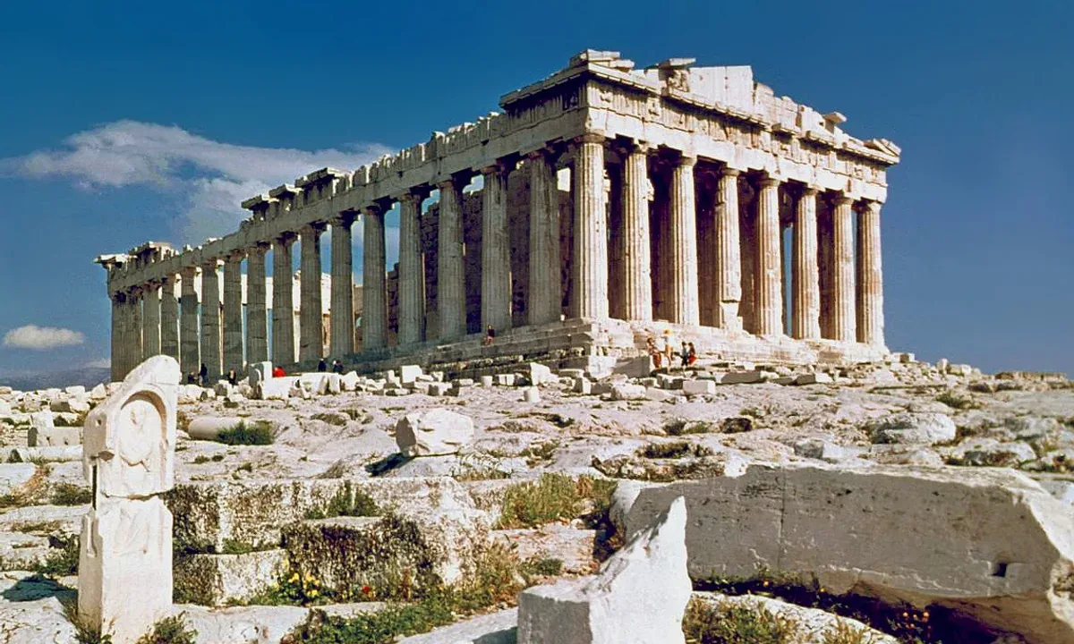 A ruined marble Doric temple with rows of columns on a rocky hilltop under a blue sky.