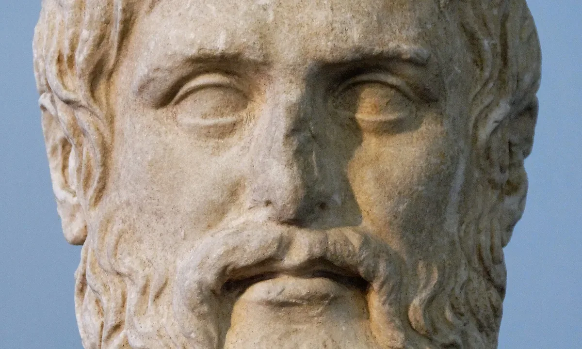 Marble head of a bearded man with wavy hair and a calm, serious expression against a blue background.