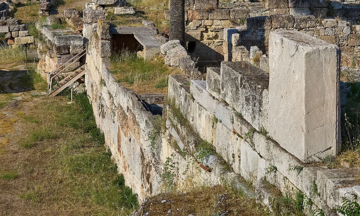 Remains of a thick ancient wall of large stone blocks running through an excavated site, with grass and a palm tree.