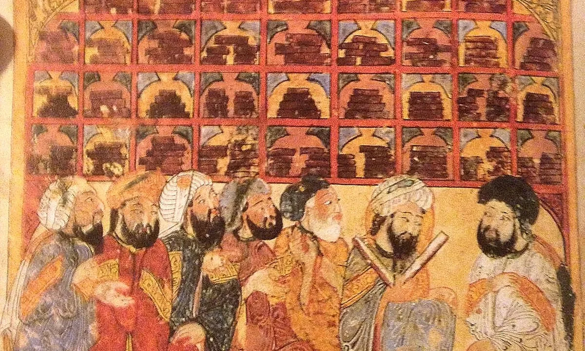 Seven turbaned, bearded men in colourful robes sit in a row in front of tall shelves stacked with books under an ornamented roof.