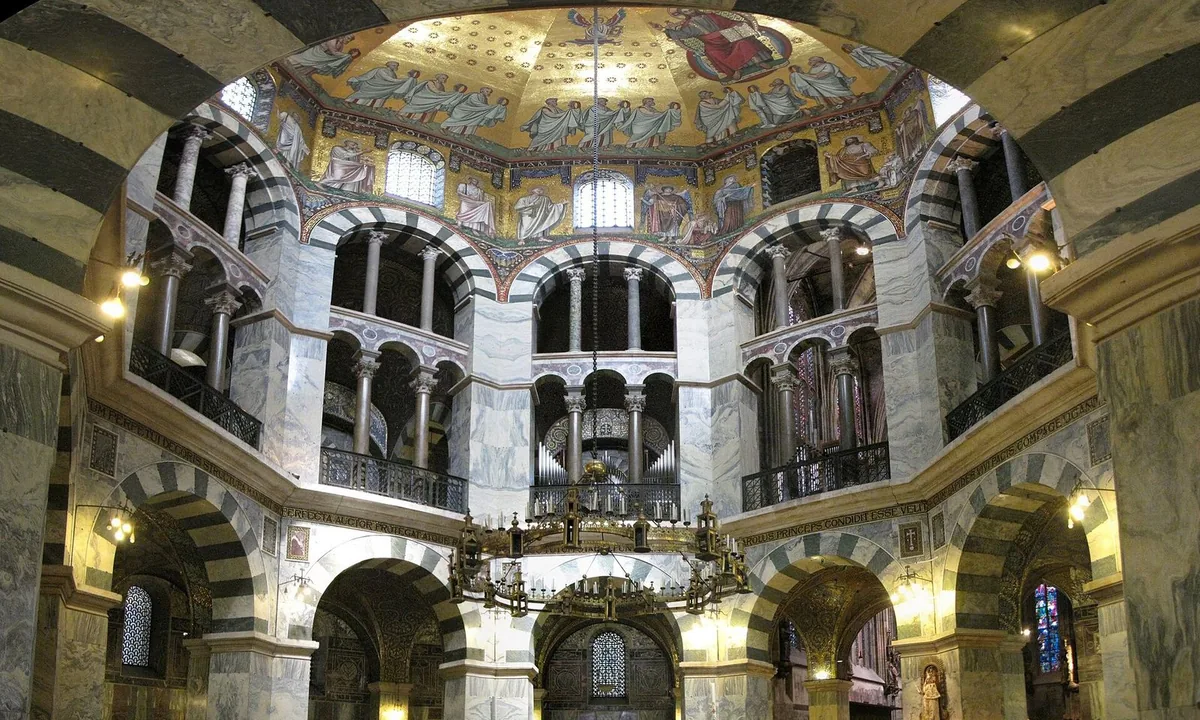 Interior of an octagonal domed chapel with tiers of round arches, marble columns and a large hanging chandelier.