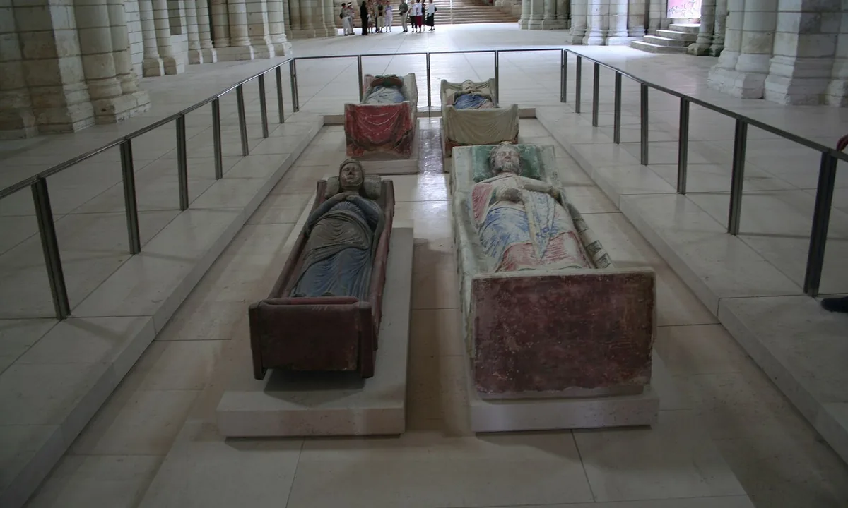 Interior of a pale stone Romanesque church with four painted tomb effigies laid out in two rows behind a low railing.