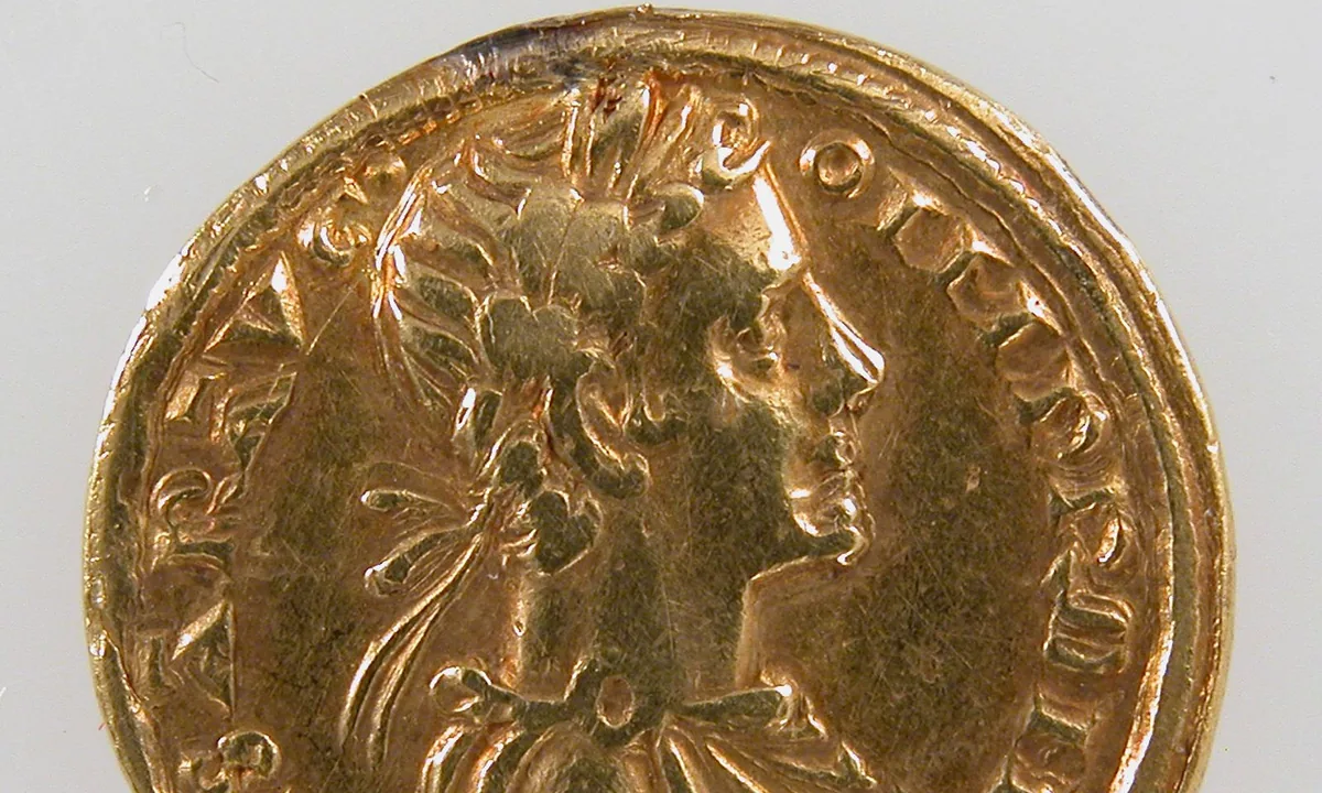 Close photograph of a small gold coin showing the profile bust of a laurel-wreathed emperor in a draped cloak, with Latin letters around the rim.