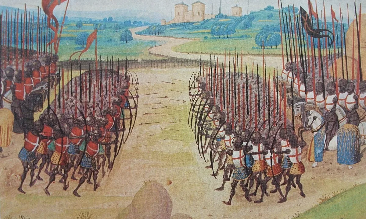 Medieval manuscript painting of two armies of archers drawing longbows at each other across a sandy field, with mounted knights and banners behind them and a castle in the distance.