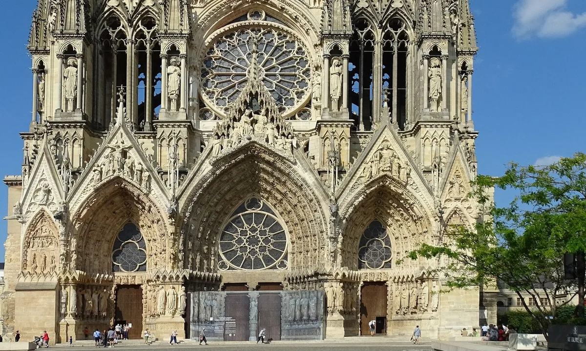 Tall Gothic cathedral façade covered in sculpture, with a rose window above three deep portals.