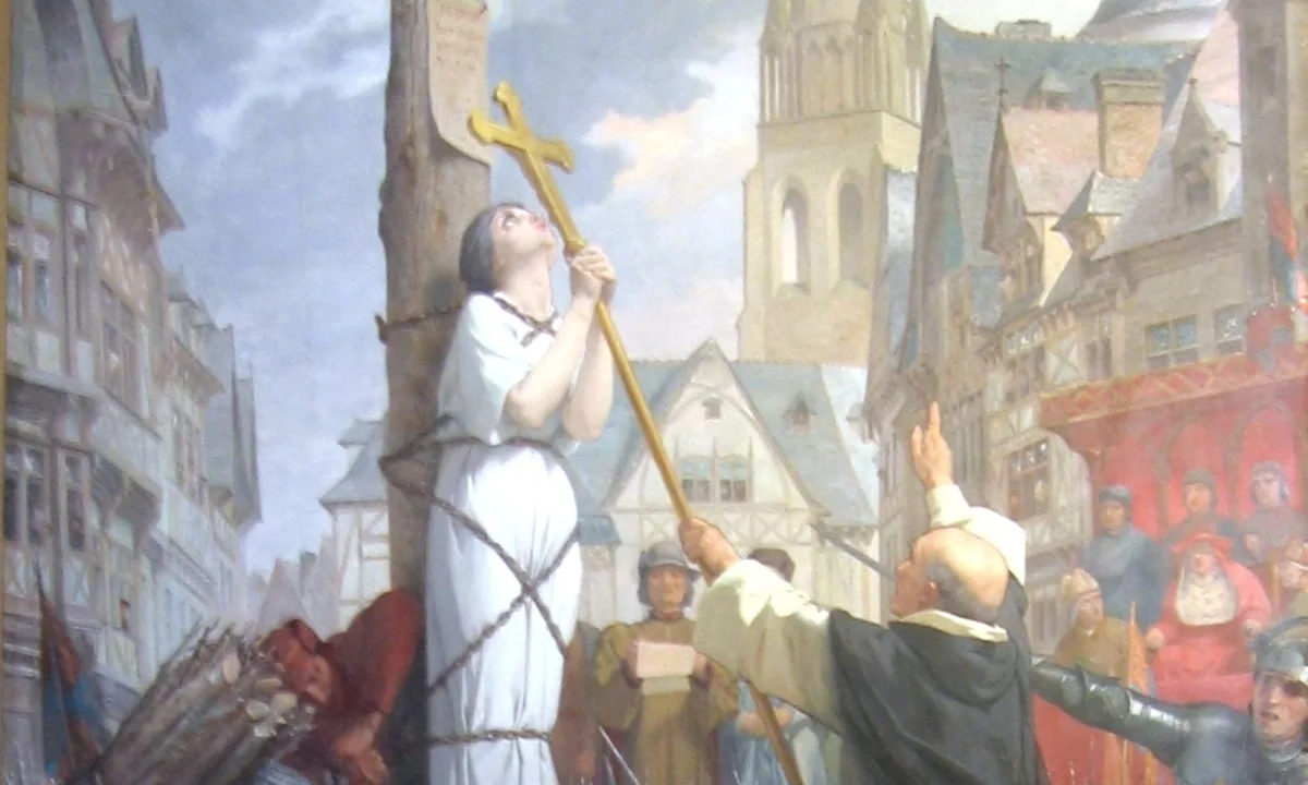 Painting of a young woman in a white dress chained to a tall stake, gazing up at a cross a monk holds out to her, with soldiers, clerics and a crowd in a medieval town square.