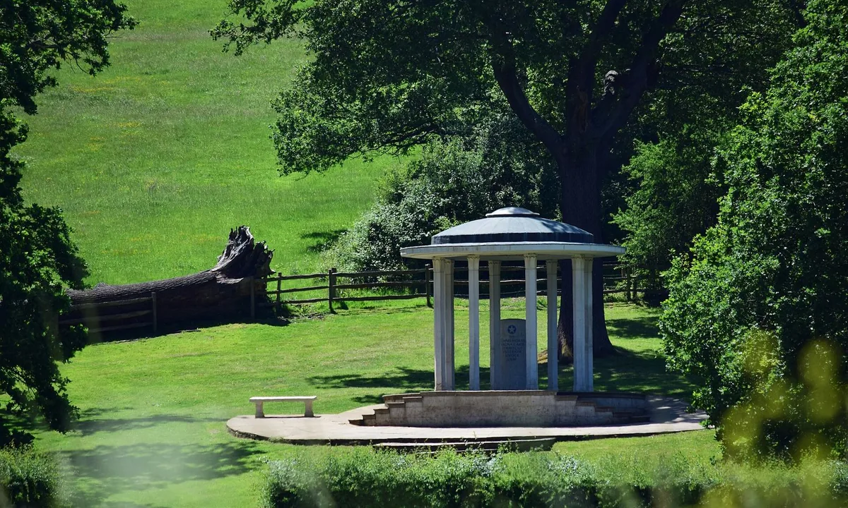 Small round classical pavilion with slender columns and a shallow dome, standing on a grassy slope among trees.