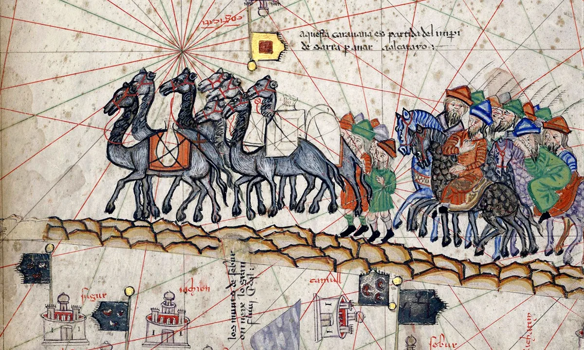 Medieval map painting of a line of grey camels loaded with packs, followed by bearded riders in pointed caps on horseback, crossing a band of rocky ground between small castles and lines of map text.