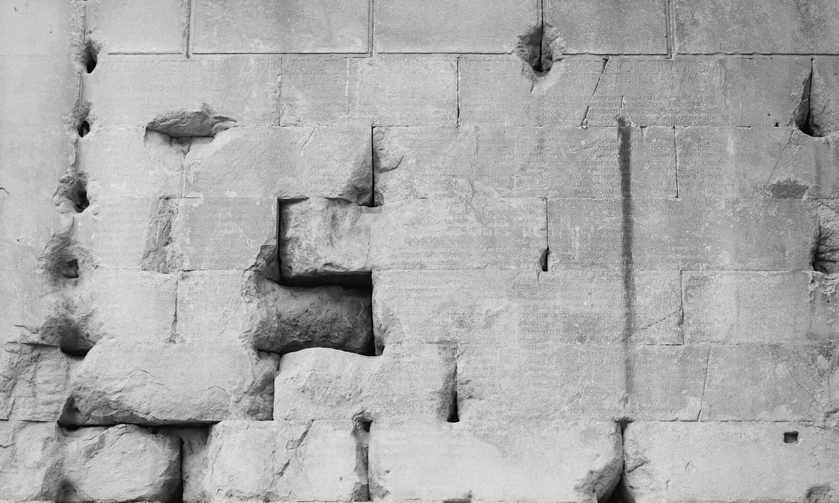 Wall of a ruined stone temple covered in long columns of carved Latin text.
