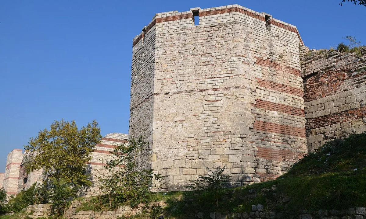 Massive stone and brick city walls with square towers running across green ground.
