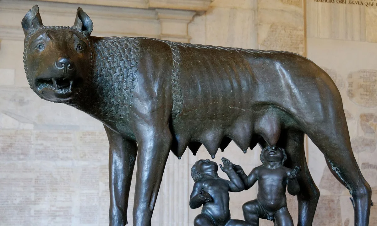 Bronze statue of a lean she-wolf with bared teeth standing over two small naked infants who reach up to suckle.
