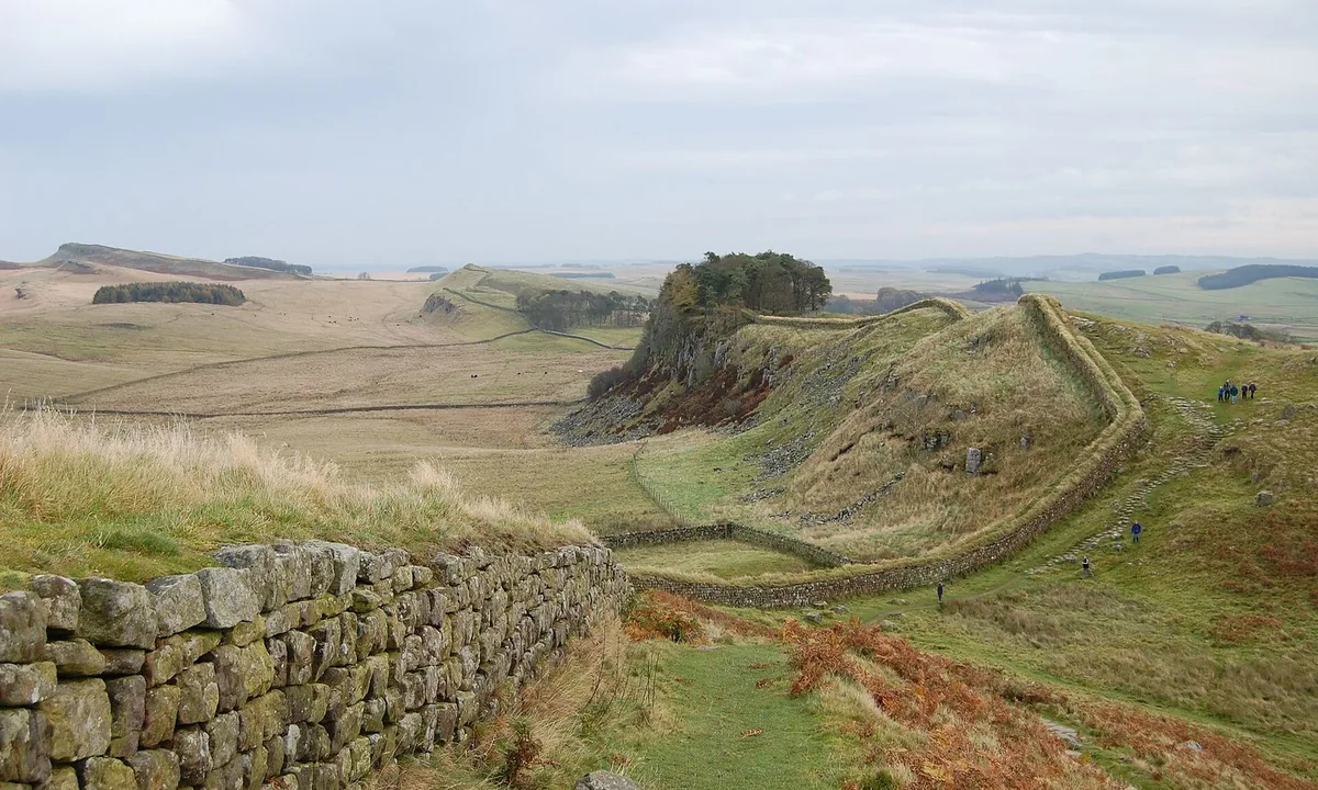 A line of stone wall running along a high ridge of green hills and crags under a cloudy sky.