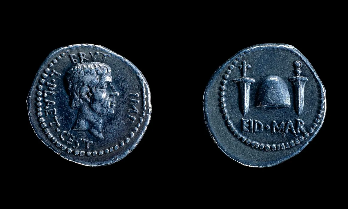 Silver coin showing a cone-shaped cap between two daggers above the letters EID MAR.