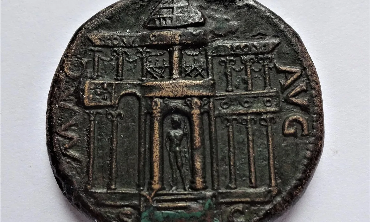 Dark bronze coin showing the front of a two-storey columned building with a domed top and a statue in its central doorway, with the letters MAC and AVG on either side.