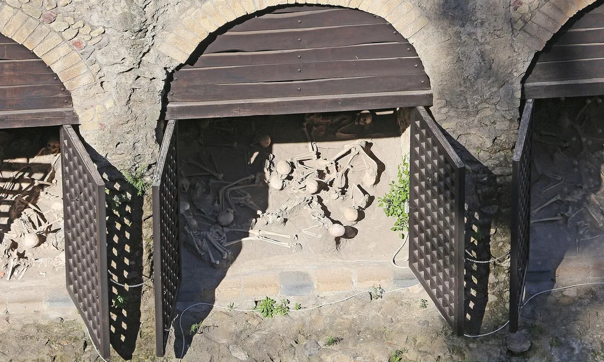 Arched openings in an ancient stone wall, with modern wooden doors swung open and human skeletons lying on the sandy floor inside.