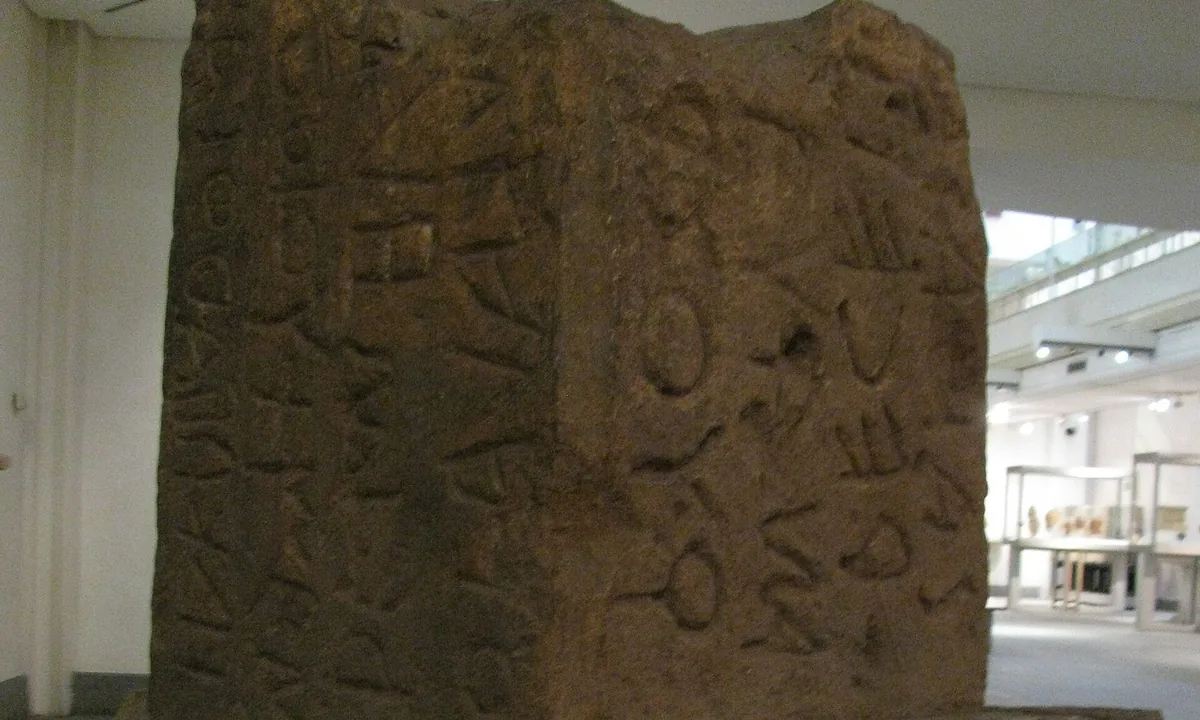 Weathered stone pillar carved with archaic letters running in alternating directions.