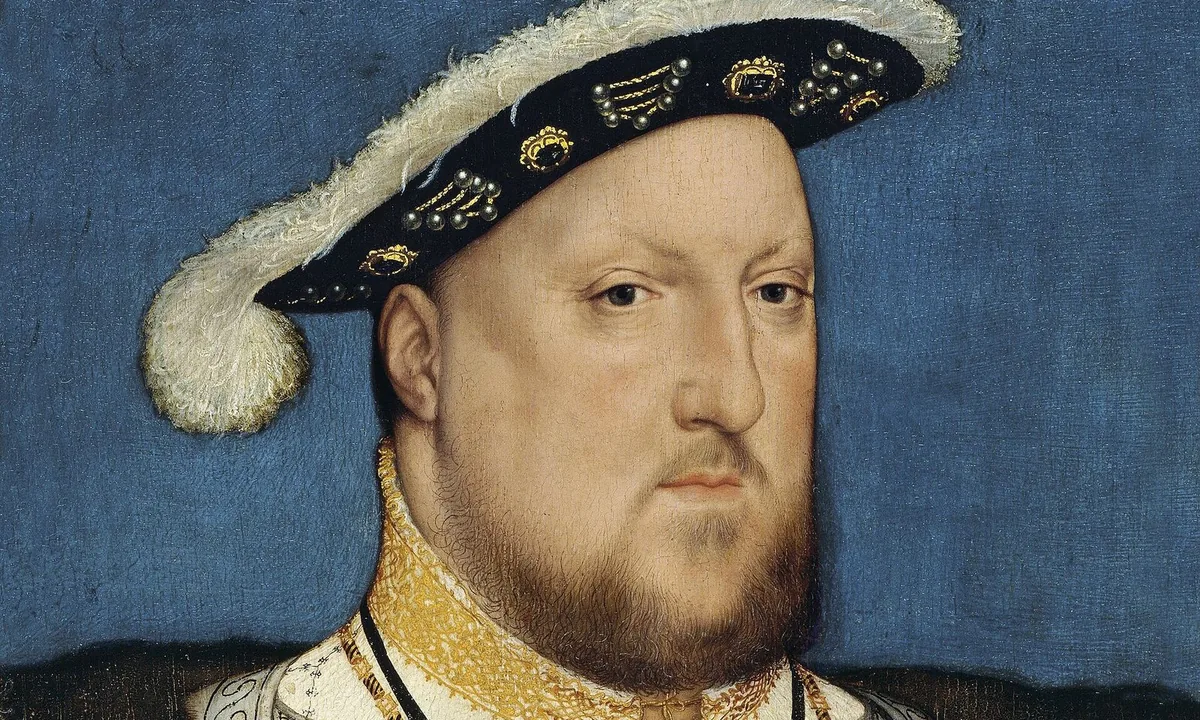 Half-length portrait of a heavy-faced bearded man in a black feathered hat and a jewelled grey-and-gold doublet, against a blue background.