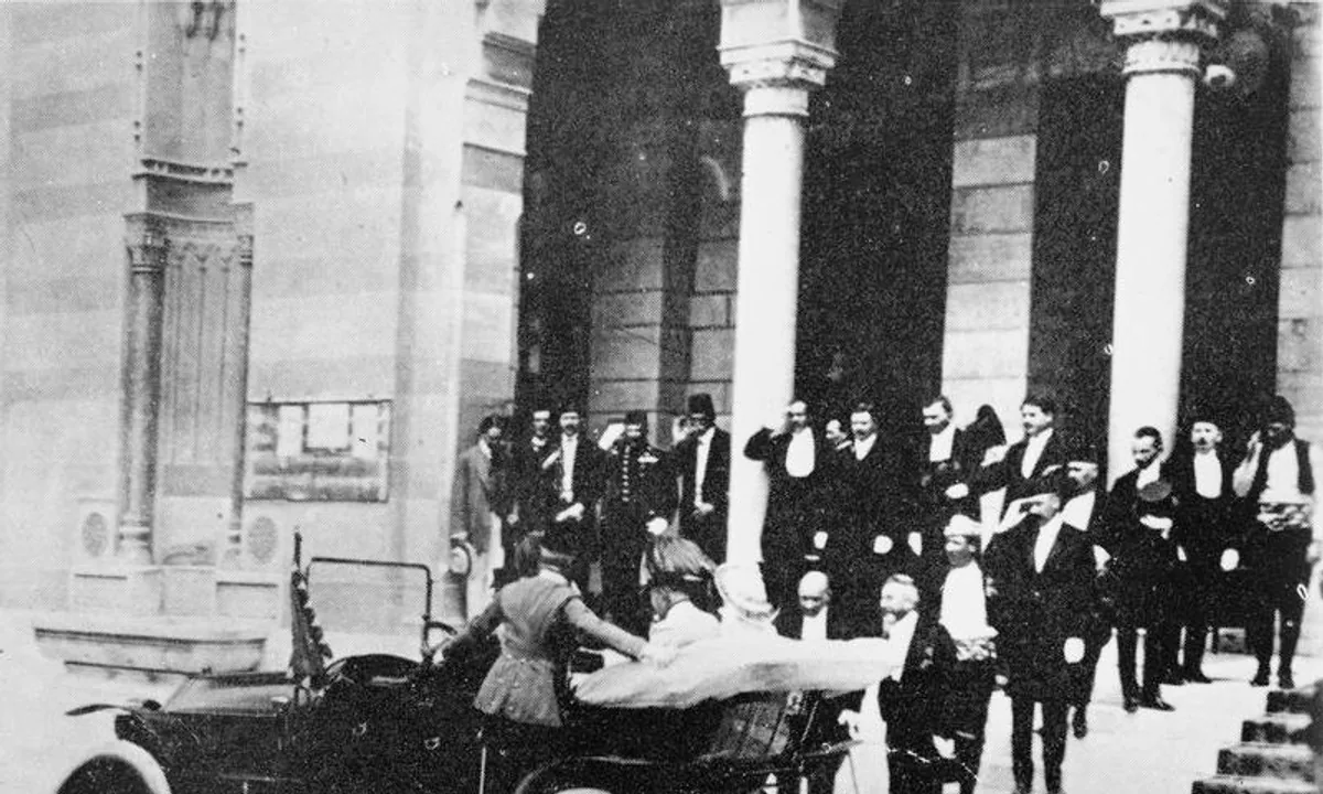 Black-and-white photo of a crowd of officials in fezzes and uniforms on the steps of a building as a couple climbs into an open car.
