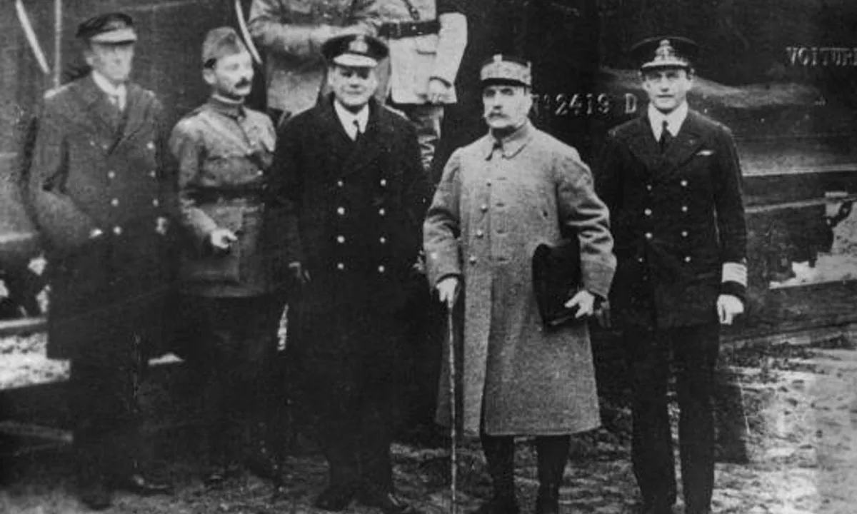 Black-and-white photo of a group of officers in French and British uniforms standing in front of a dark railway carriage in a wood.