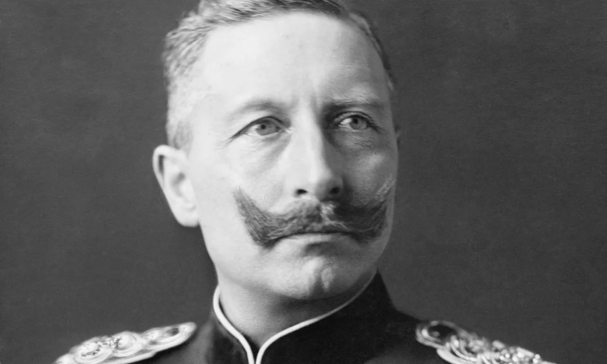 Black-and-white portrait of a man with an upturned moustache in a dark military tunic with epaulettes and a cross-shaped order at the collar.