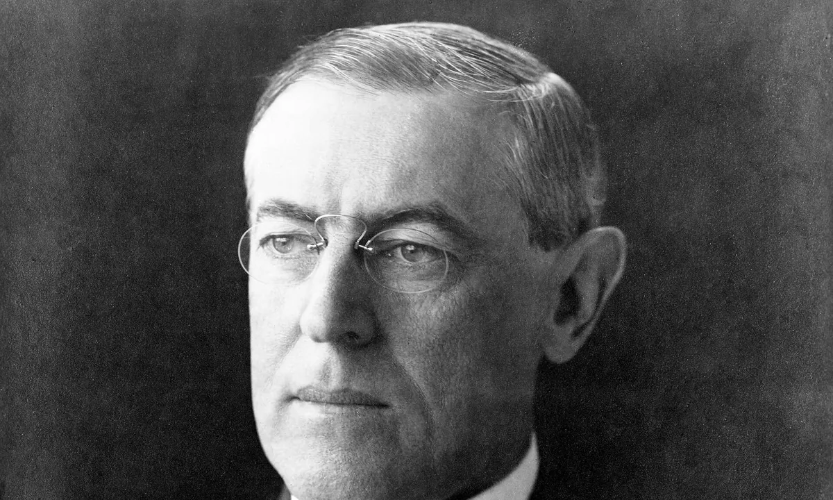 Black-and-white studio portrait of a man in rimless pince-nez glasses, dark suit and tie, looking to the left.